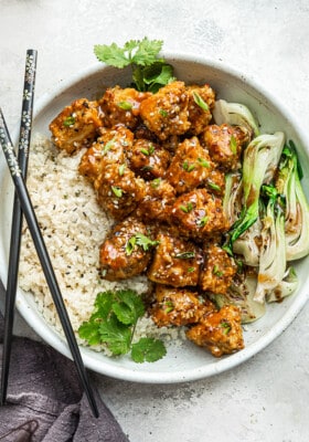 Crispy teriyaku tofu in a bowl with a side of bok choy and cauliflower rice with chopsticks