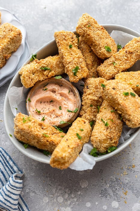 Side view of a pile of tofu fries in a an oval dish with creamy spicy dip