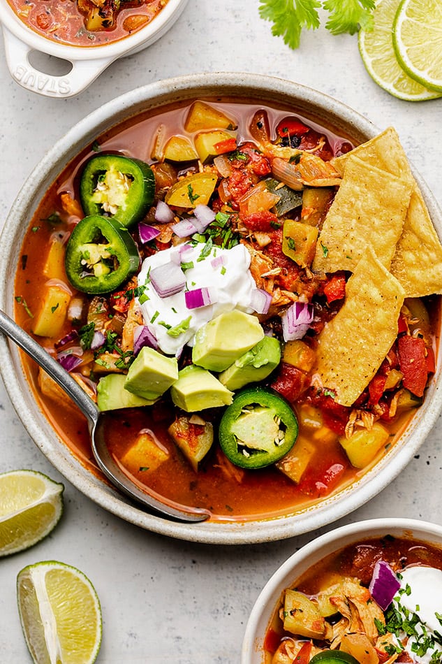 A metal spoon digging into a bowl of chicken tortilla soup finished off with fresh veggies and coconut cream