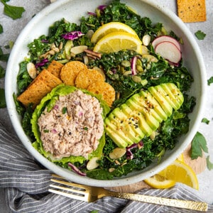 A kale salad with tuna, avocado and cheese crackers in a white bowl
