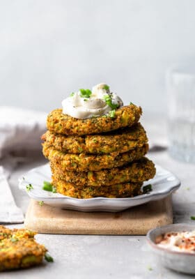 Far side view of a stack of five vegan broccoli fritters on a white plate with coconut cream