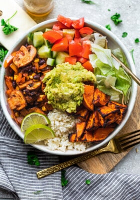 A vegan burrito bowl on a wooden cutting board beside a striped kitchen towel