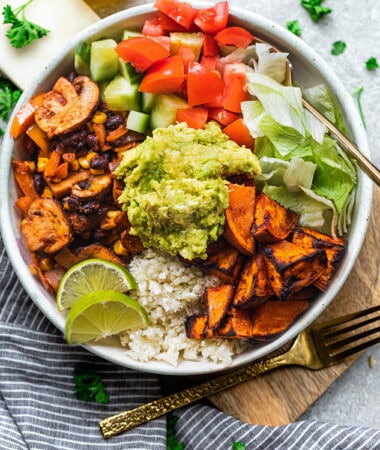 A vegan burrito bowl on a wooden cutting board beside a striped kitchen towel