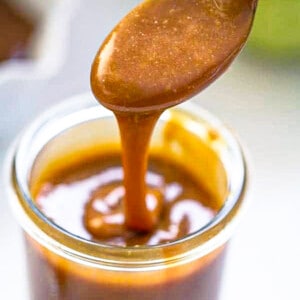 Close-up shot of a spoonful of easy caramel sauce over a jar