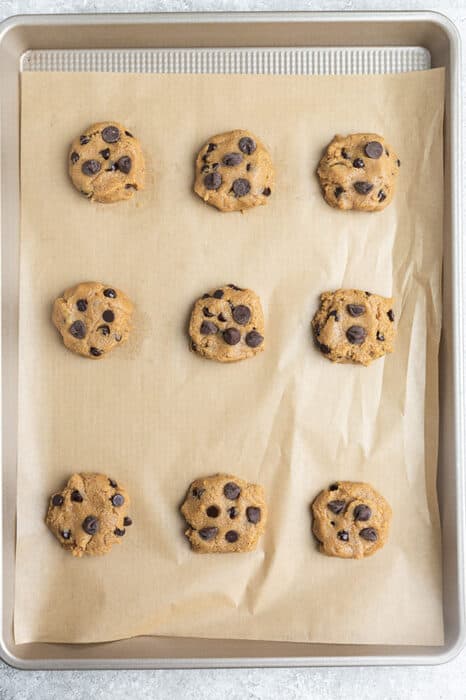 Top view of nine unbaked gluten free chocolate chip cookies on a parchment paper on a baking sheet