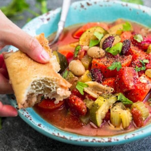 A bowl of vegetarian minestrone soup in a blue bowl with a serving of Italian bread