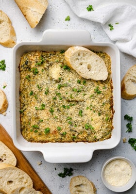 Vegan Spinach Artichoke Dip in a white square baking pan with a toasted baguette