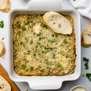 Vegan Spinach Artichoke Dip in a white square baking pan with a toasted baguette