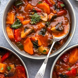 Top view of 3 bowls of vegetable stew on a grey background