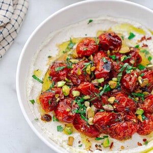 Whipped cottage cheese in a white owl topped with roasted tomatoes and pistachios