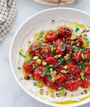 Whipped cottage cheese in a white owl topped with roasted tomatoes and pistachios