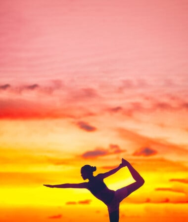 Yoga silhouette of woman stretching doing dancers pose in beautiful dusk colors at sunset on beach background. Copy space on pink sky clouds. Wellness meditation concept.