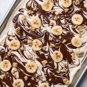 Overhead view of yogurt topped with melted chocolate swirls, banana slices and granola
