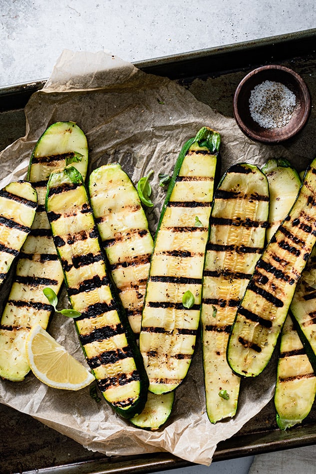 Top view of grilled zucchini slices on a parchment paper on a baking sheet