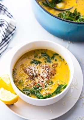One serving of zuppa toscana soup in a white bowl with lemon wedges