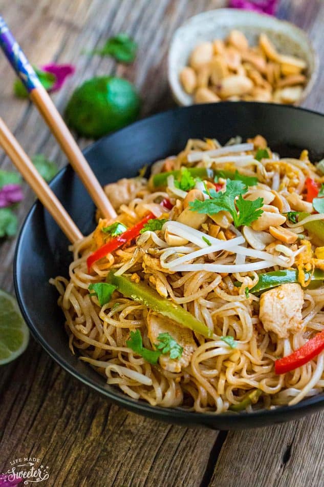 Chicken Pad Thai rice noodles with red bell peppers, carrots and peanuts in a large black bowl on a wooden table.