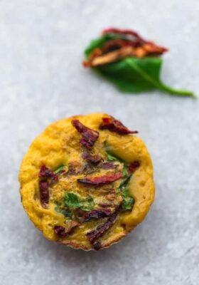 Top view of Egg Cups with sun-dried tomato and spinach on a grey background