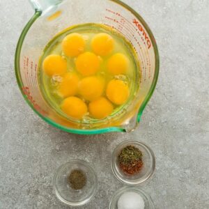 Top view of eggs and seasonings in a measuring cup and clear pinch bowls to make Egg Muffins