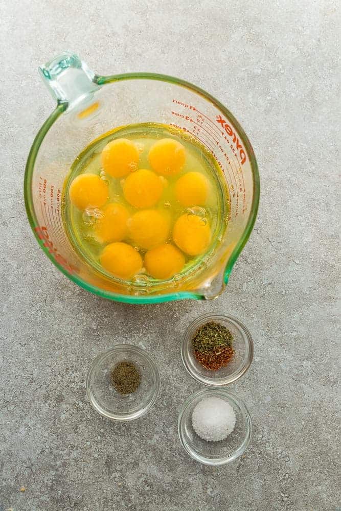 Top view of eggs and seasonings in a measuring cup and clear pinch bowls to make Egg Muffins