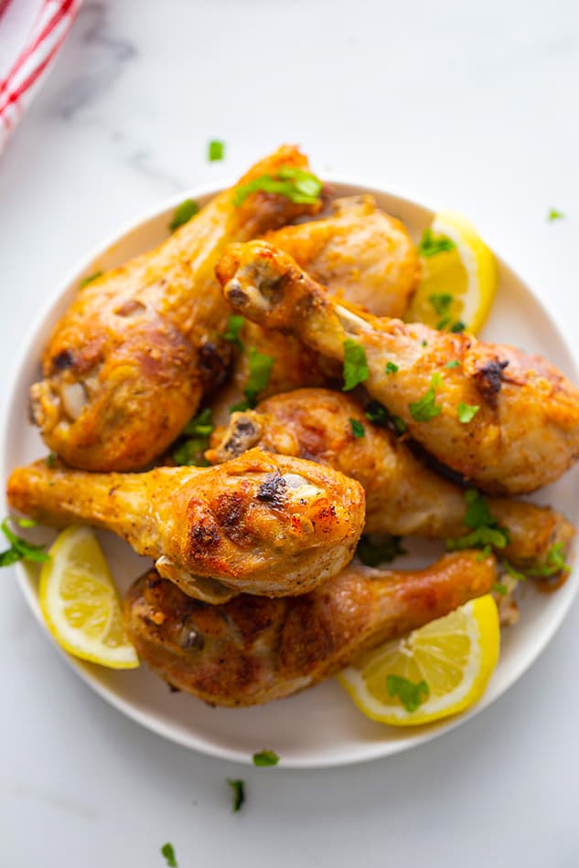A bowl of crispy air fryer drumsticks with parsley and lemon
