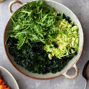 Overhead view of massaged kale, arugula and shaved Brussels sprouts in a round serving bowl.