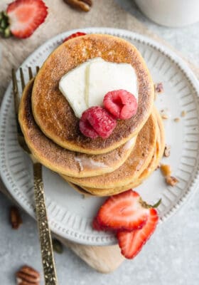 Top view of four coconut flour pancakes on a white plate with berries and syrup