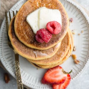 Top view of four coconut flour pancakes on a white plate with berries and syrup