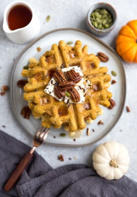 Top view of a stack of thick and fluffy Keto Pumpkin Waffles on a white plate with a fork and knife