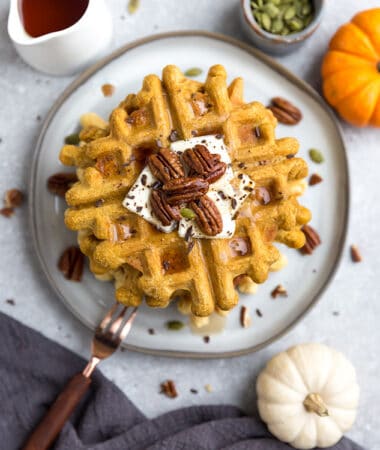 Top view of a stack of thick and fluffy Keto Pumpkin Waffles on a white plate with a fork and knife