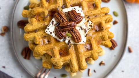 Top view of a stack of thick and fluffy Keto Pumpkin Waffles on a white plate with a fork and knife