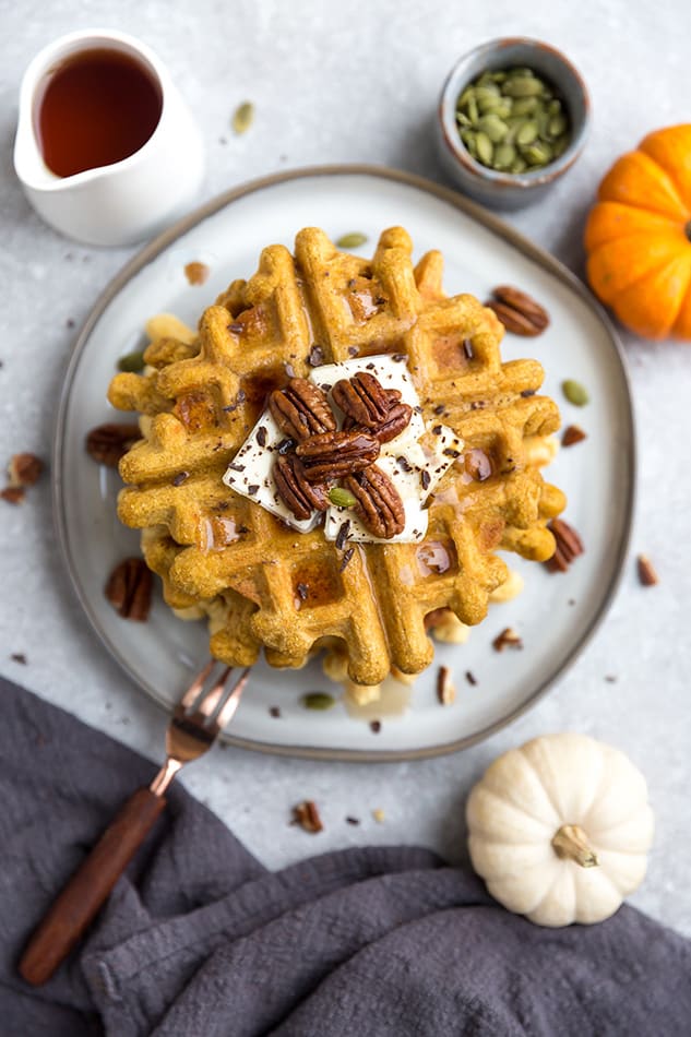 Top view of a stack of thick and fluffy Keto Pumpkin Waffles on a white plate with a fork and knife