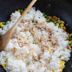 Cooked rice, mixed vegetables, scrambled eggs and the rest of the elements being combined in a large pan