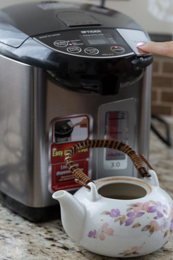 A ceramic tea pot next to a water boiler appliance