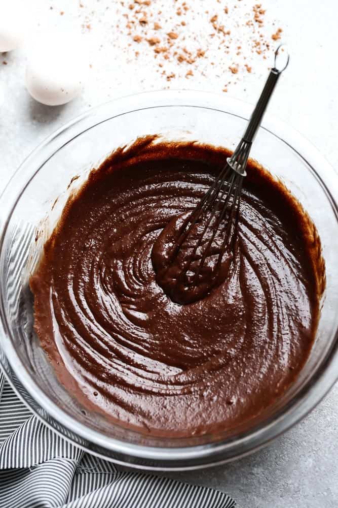 Mixing delicious Paleo Brownies batter in a clear glass mixing bowl with a whisk.