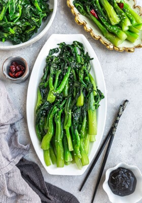 Flat lay of stir fried Chinese broccoli on a white oval plate with black chopsticks
