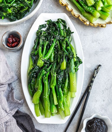 Flat lay of stir fried Chinese broccoli on a white oval plate with black chopsticks