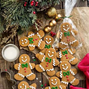 Top view of a batch of decorated gingerbread men cookies on a wooden board surrounded by a mistletoe and bells.