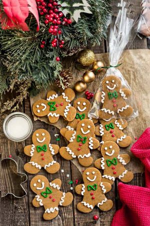Top view of a batch of decorated gingerbread men cookies on a wooden board surrounded by a mistletoe and bells.