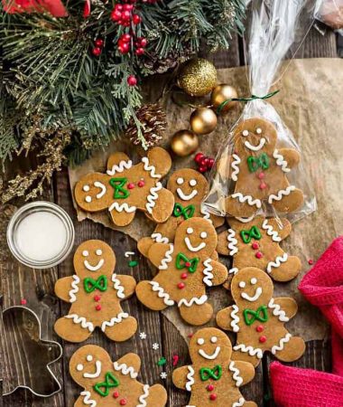Top view of a batch of decorated gingerbread men cookies on a wooden board surrounded by a mistletoe and bells.