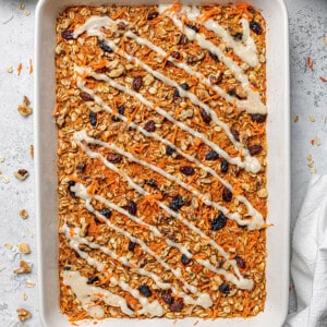 Carrot Cake Baked Oatmeal Batter in a white casserole pan with a drizzle of vegan cream cheese frosting