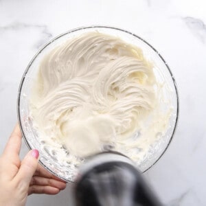 A hand holding a mixer to mix the cream cheese frosting