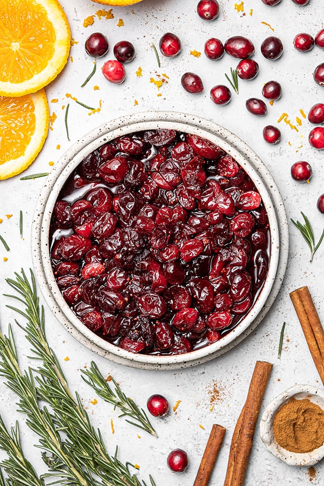 Overhead view of fresh cranberry sauce in a bowl with fresh herbs and spices nearby