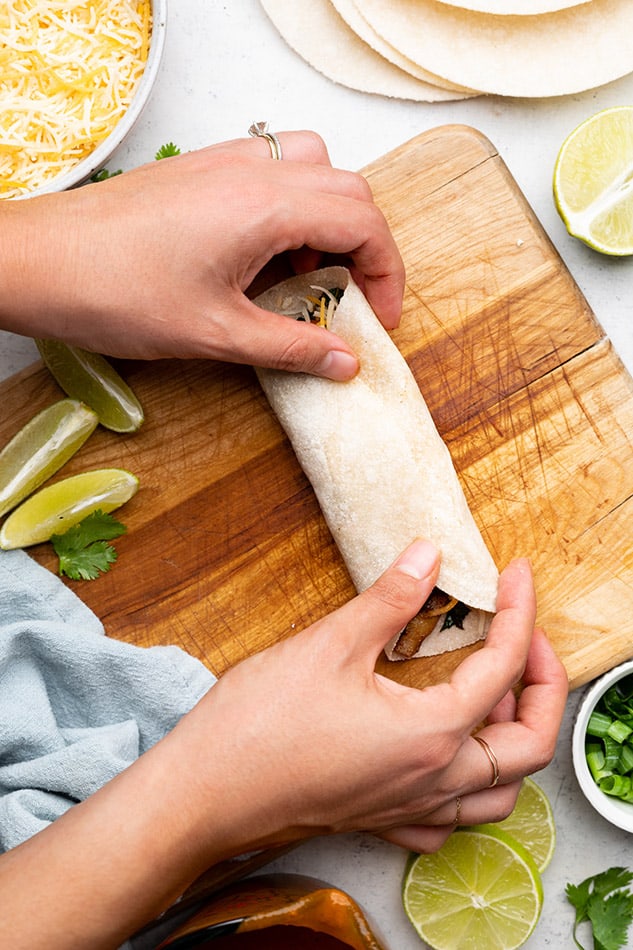A veggie enchilada being rolled up on a wooden cutting board