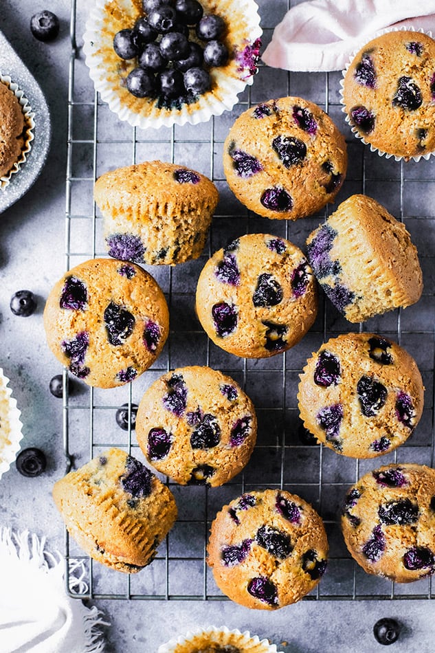 Top view of scattered keto blueberry muffins on a wire rack on a grey background with fresh blueberries