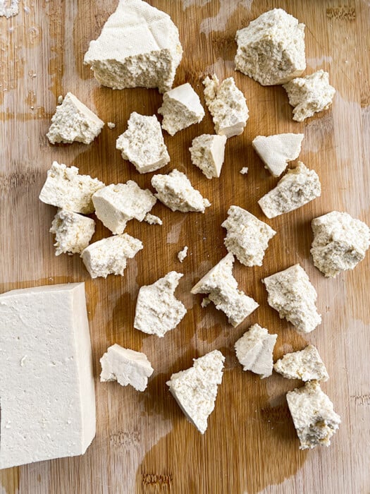 Torn tofu pieces on a wooden cutting board