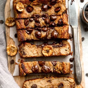 Top view of slices of paleo chocolate chip banana bread on a wooden cutting board on parchment paper with a knife