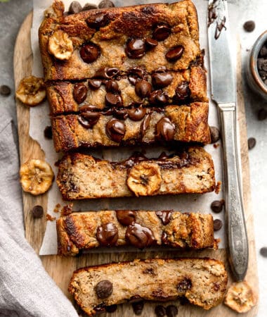 Top view of slices of paleo chocolate chip banana bread on a wooden cutting board on parchment paper with a knife