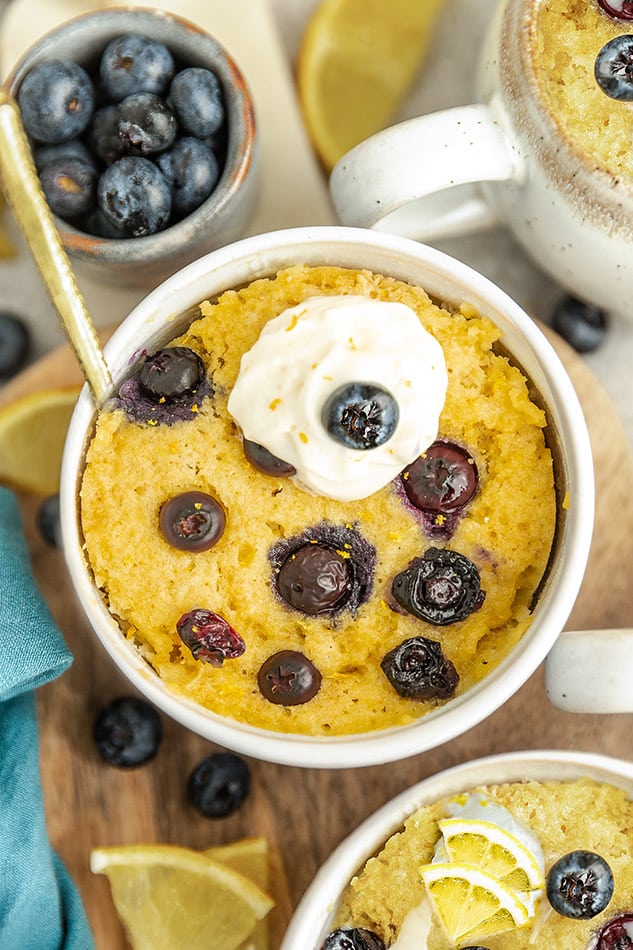 Top view of blueberry mug cake with fresh blueberries in white bowl.