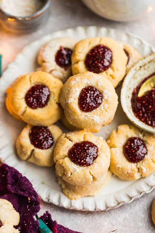 A plate full of thumbprint cookies filled with berry jam, next to a bowl of jam