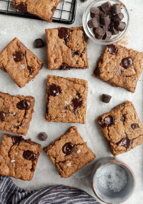Top view of 8 scattered paleo blondies chocolate chip cookie bars on a white background